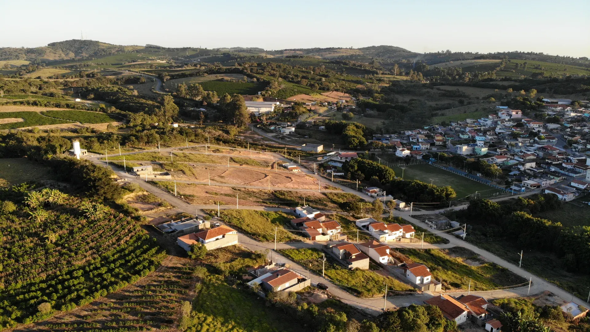 Aérea ampla do Residencial Bela Vista junto a São Sebastião da Estrela, mostrando o loteamento aberto, o distrito consolidado e as colinas ao redor