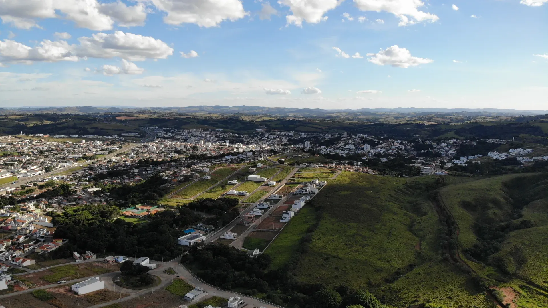 Aérea ampla do Gran Ville mostrando a integração do condomínio com o tecido urbano de Perdões e o relevo da serra ao redor