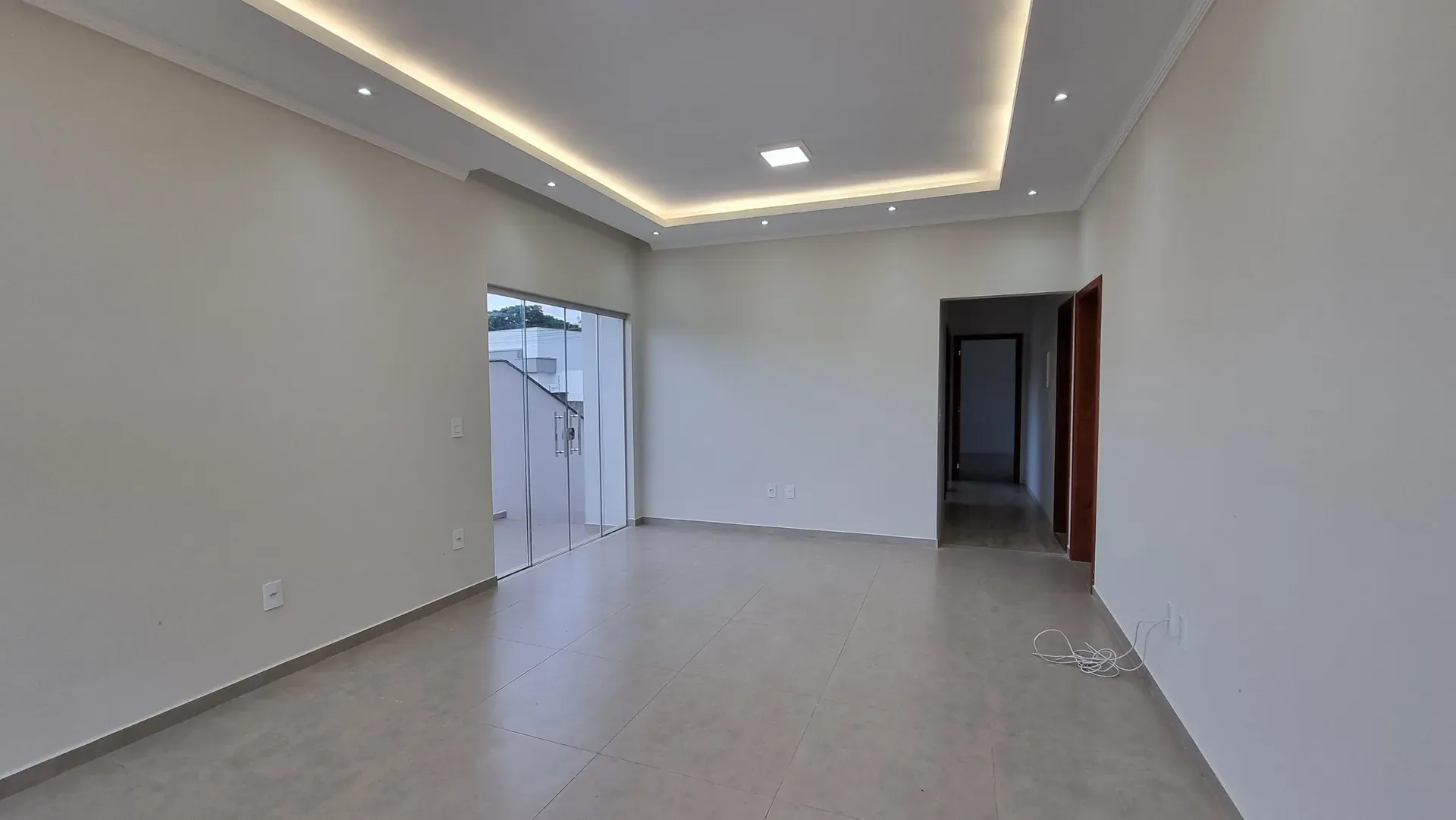 Sala de estar ampla da Casa do Gran Ville, com iluminação em sanca de gesso, porta de vidro para a área externa e piso porcelanato