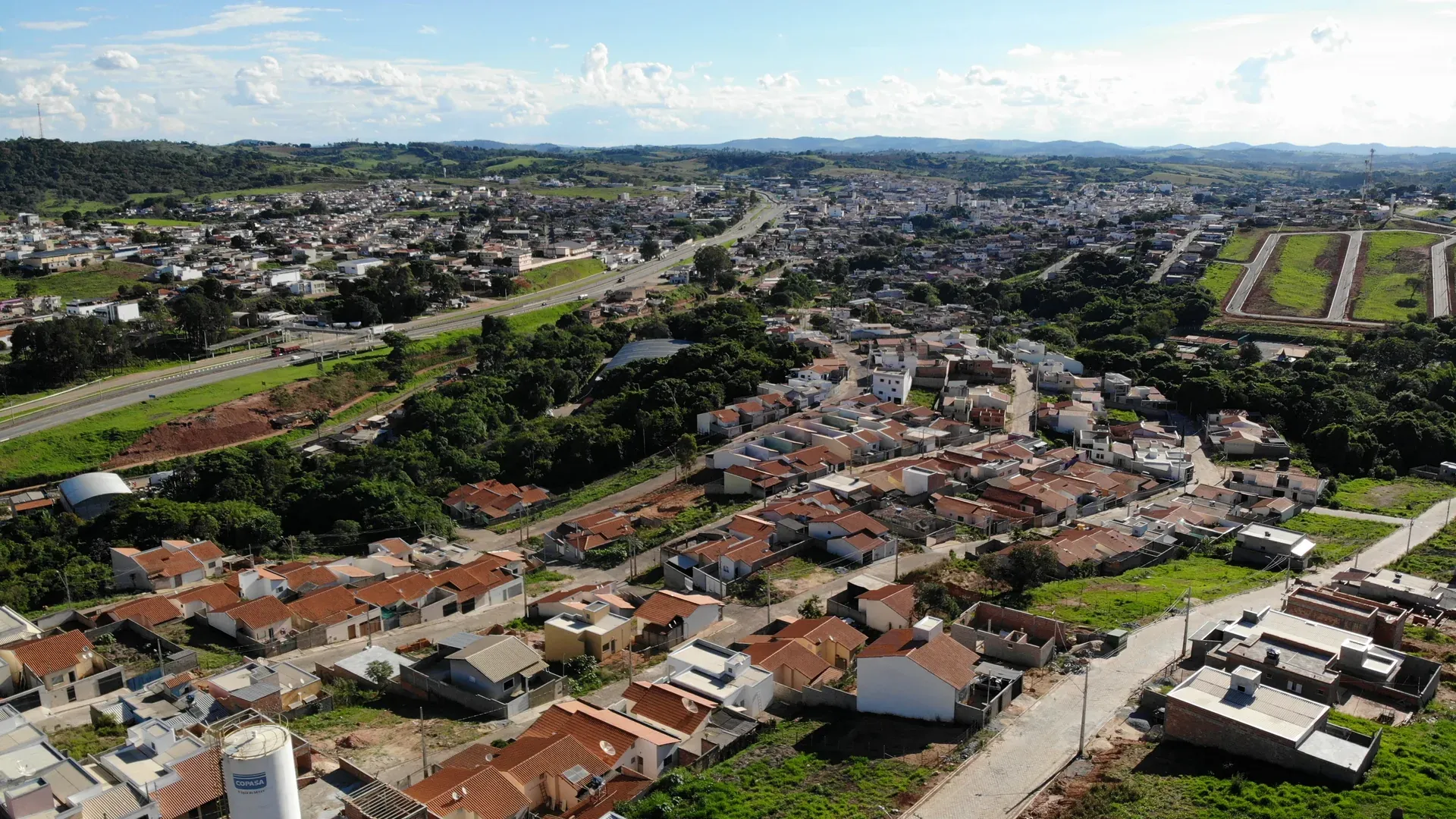 Aérea ampla do conjunto urbano do Jardim Centenário ao lado da Rodovia Fernão Dias, com Perdões consolidada ao fundo