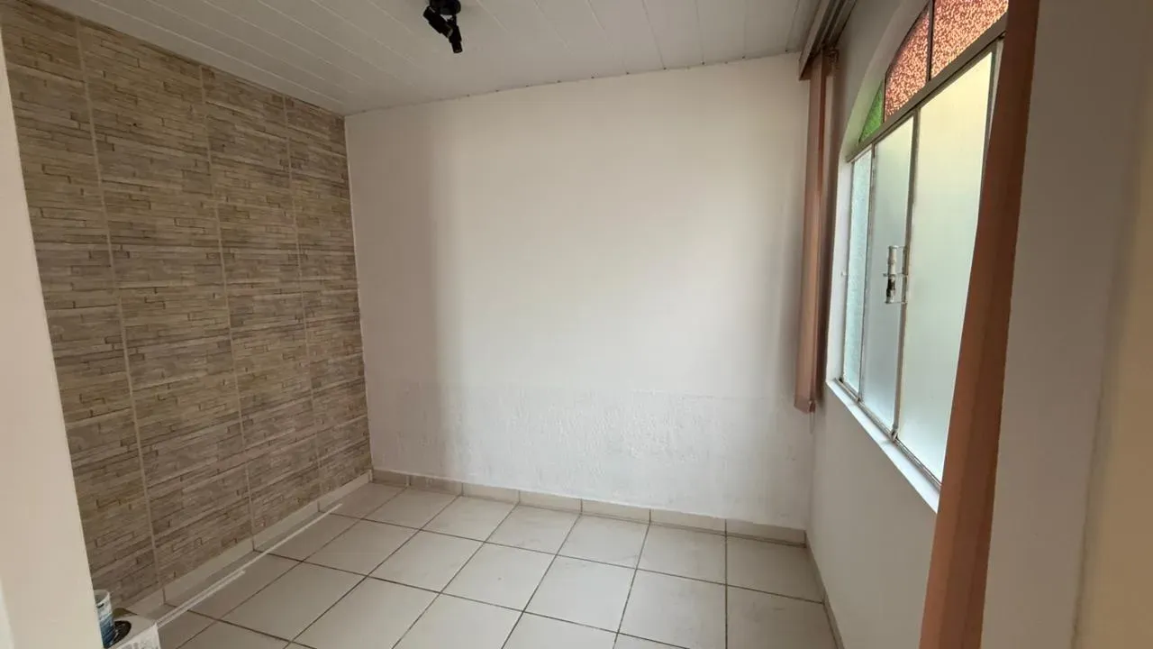 Ambiente interno da Casa do Lourdes, com parede revestida em pedra decorativa, piso cerâmico claro e janela