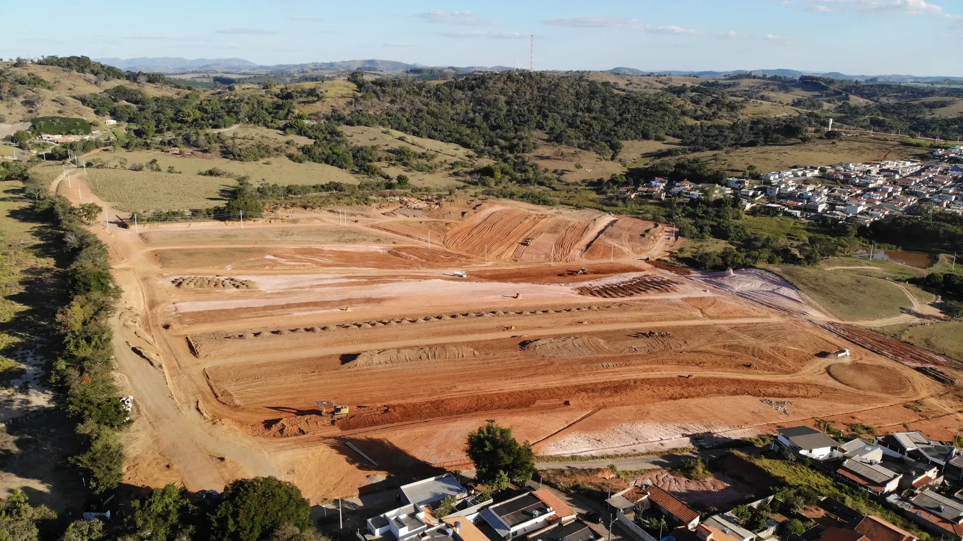 Vista aérea aproximada dos platôs de terraplenagem do Portal da Serra, com maquinário em operação e a cidade ao lado