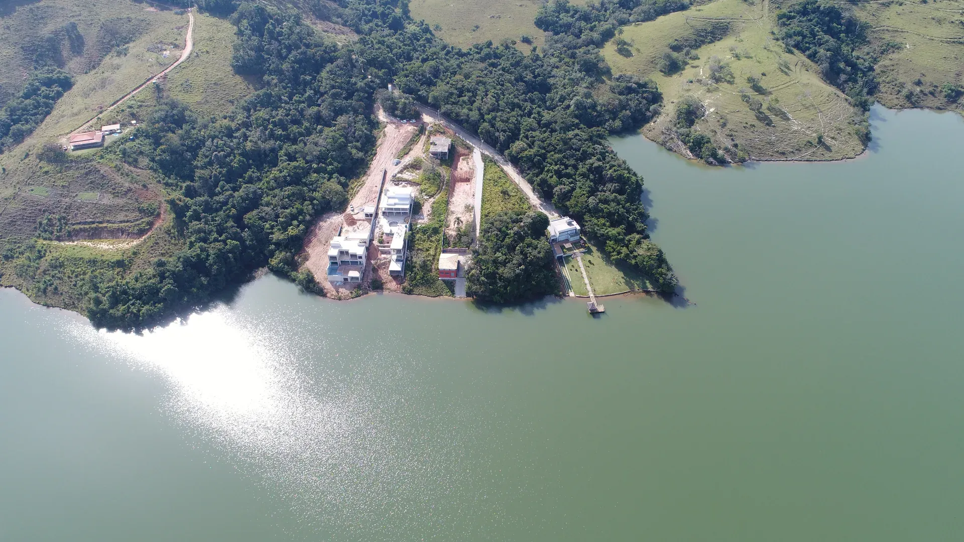 Aérea do conjunto do condomínio mostrando residências, deck na borda do lago e o reflexo prateado da água