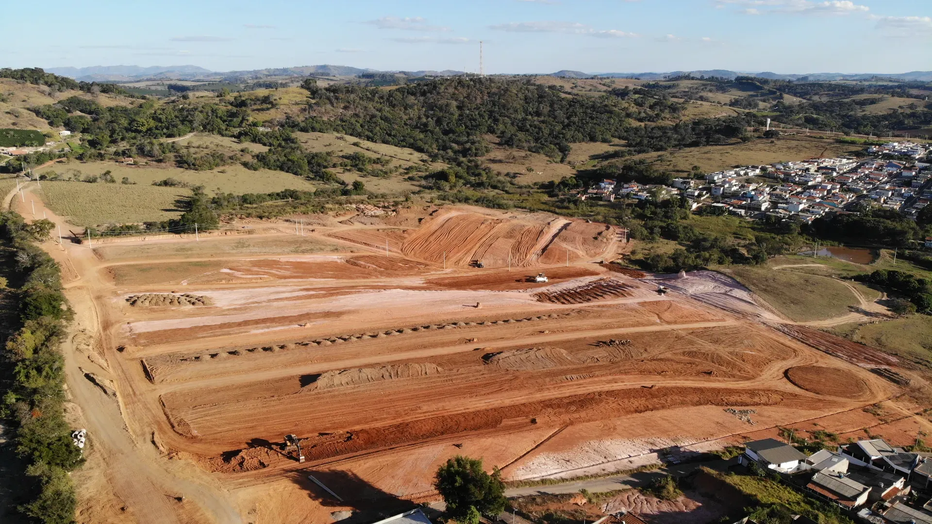 Aérea do conjunto do Portal da Serra em obras, com os platôs do loteamento, máquinas e a cidade de Perdões à direita