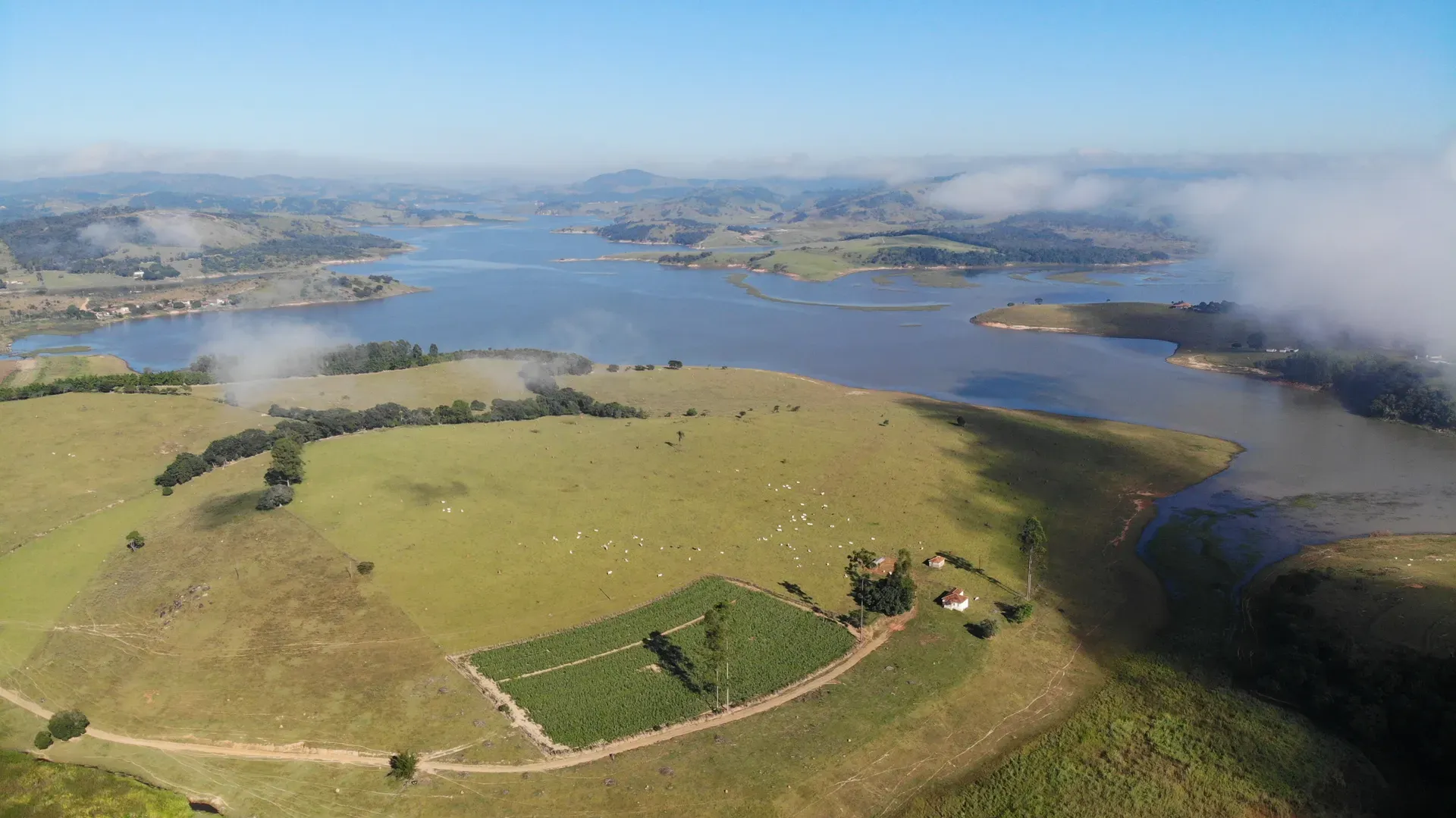 Vista panorâmica da Fazenda Coelhos às margens do lago, com sede, lavoura, pastagens e ilhas ao fundo