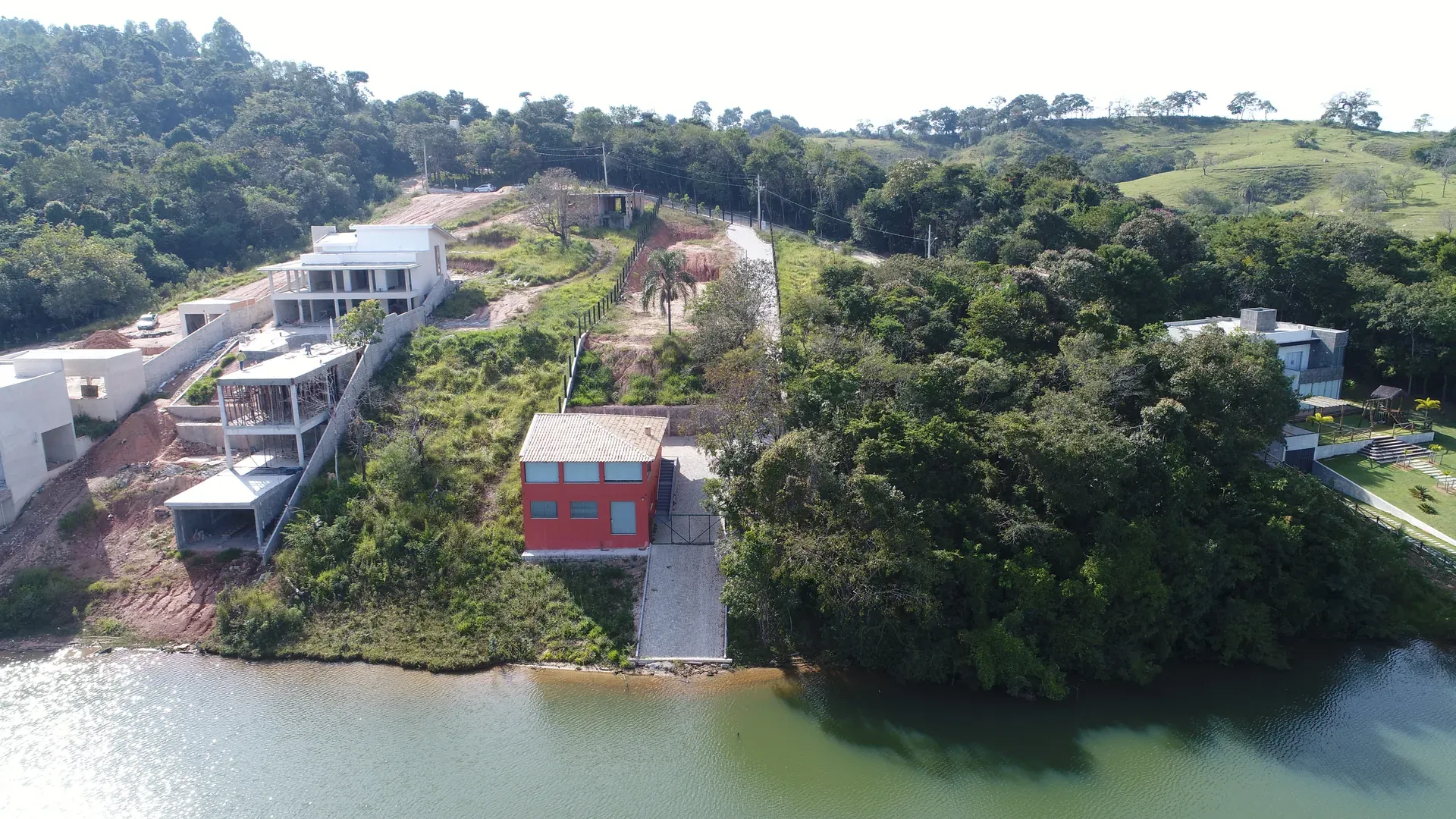 Casa moderna com telhado vermelho à beira do lago, com deck particular sobre a água e mata nativa ao redor
