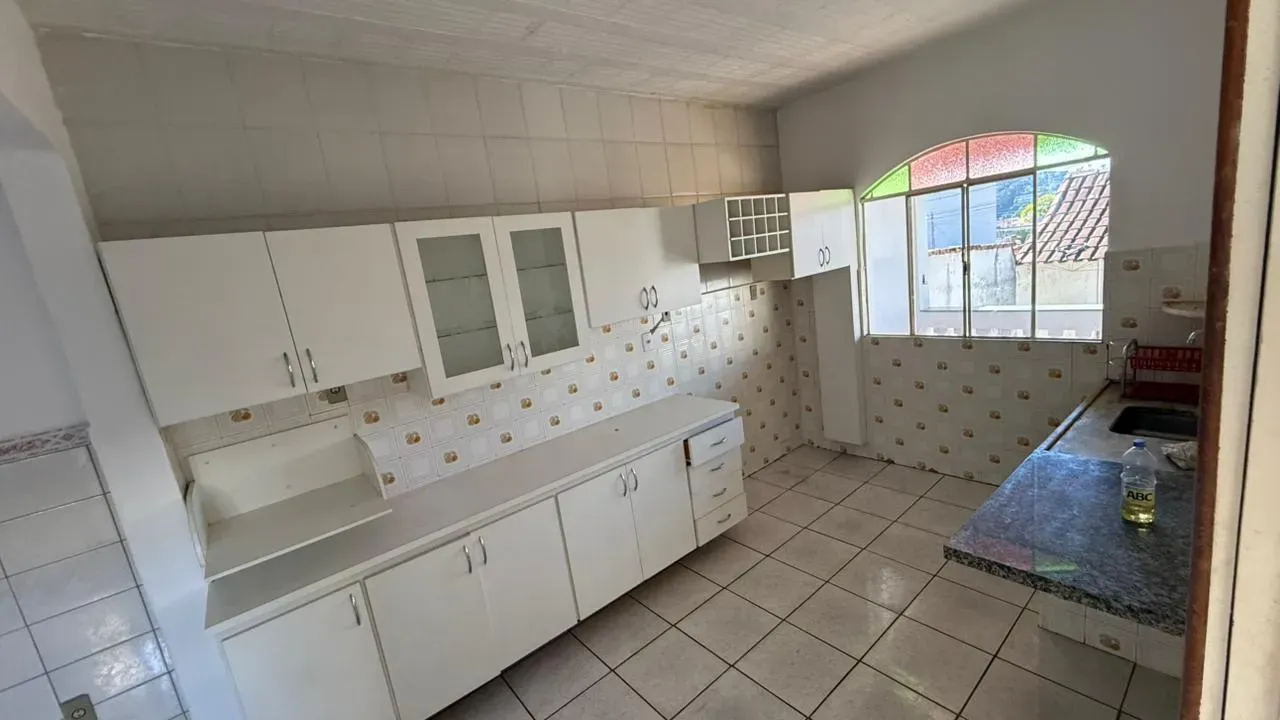 Cozinha da Casa do Lourdes com armários brancos, bancada de granito e ampla janela com vista para a rua
