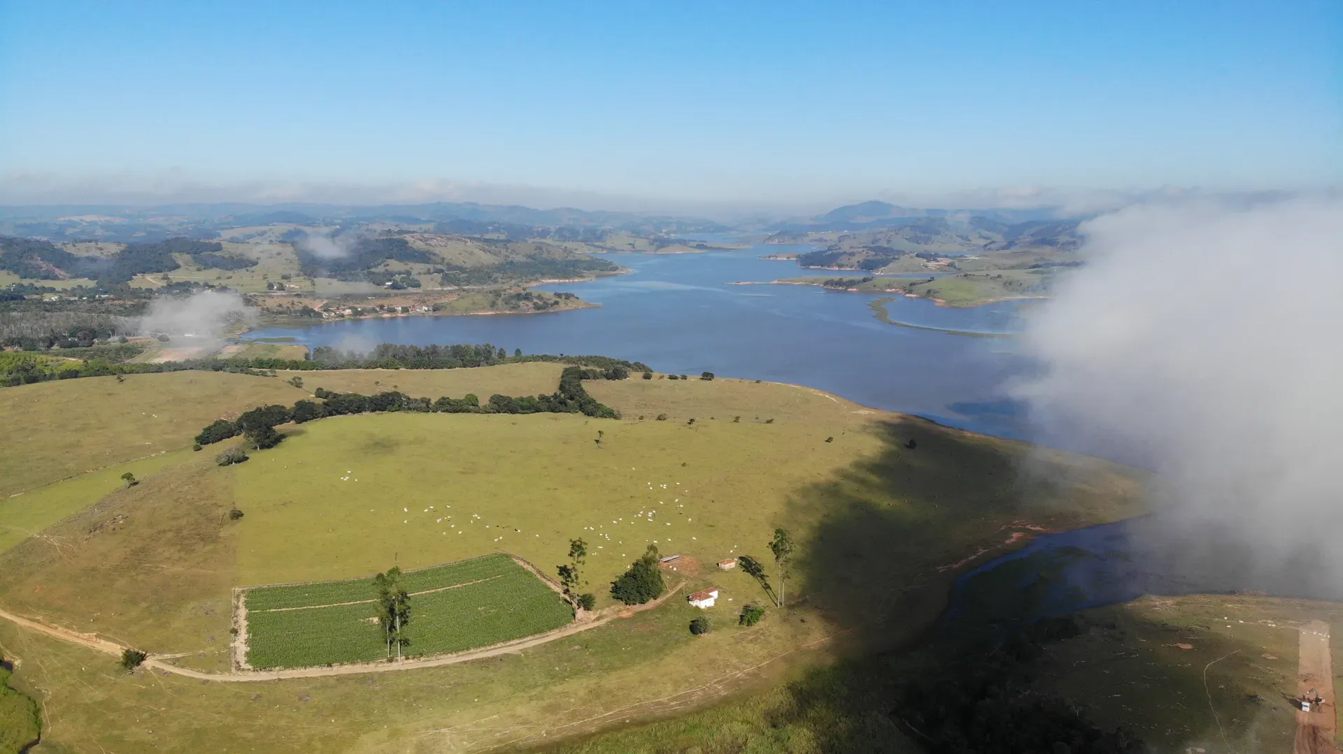 Áreas de lavoura e pastagem da Fazenda Coelhos à beira do lago, com a sede e os morros ao fundo