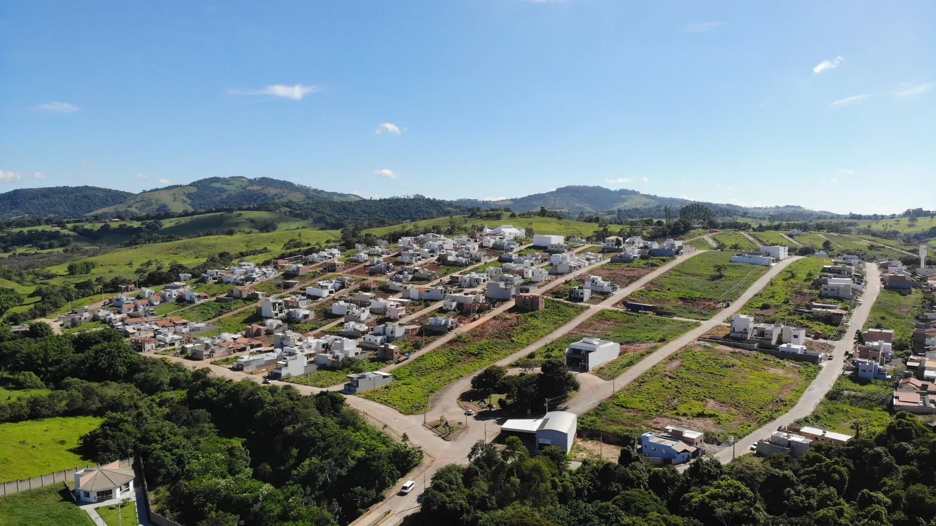 Ruas pavimentadas, lotes e casas construídas no Residencial Vila Real, com a serra do Sul de Minas ao fundo