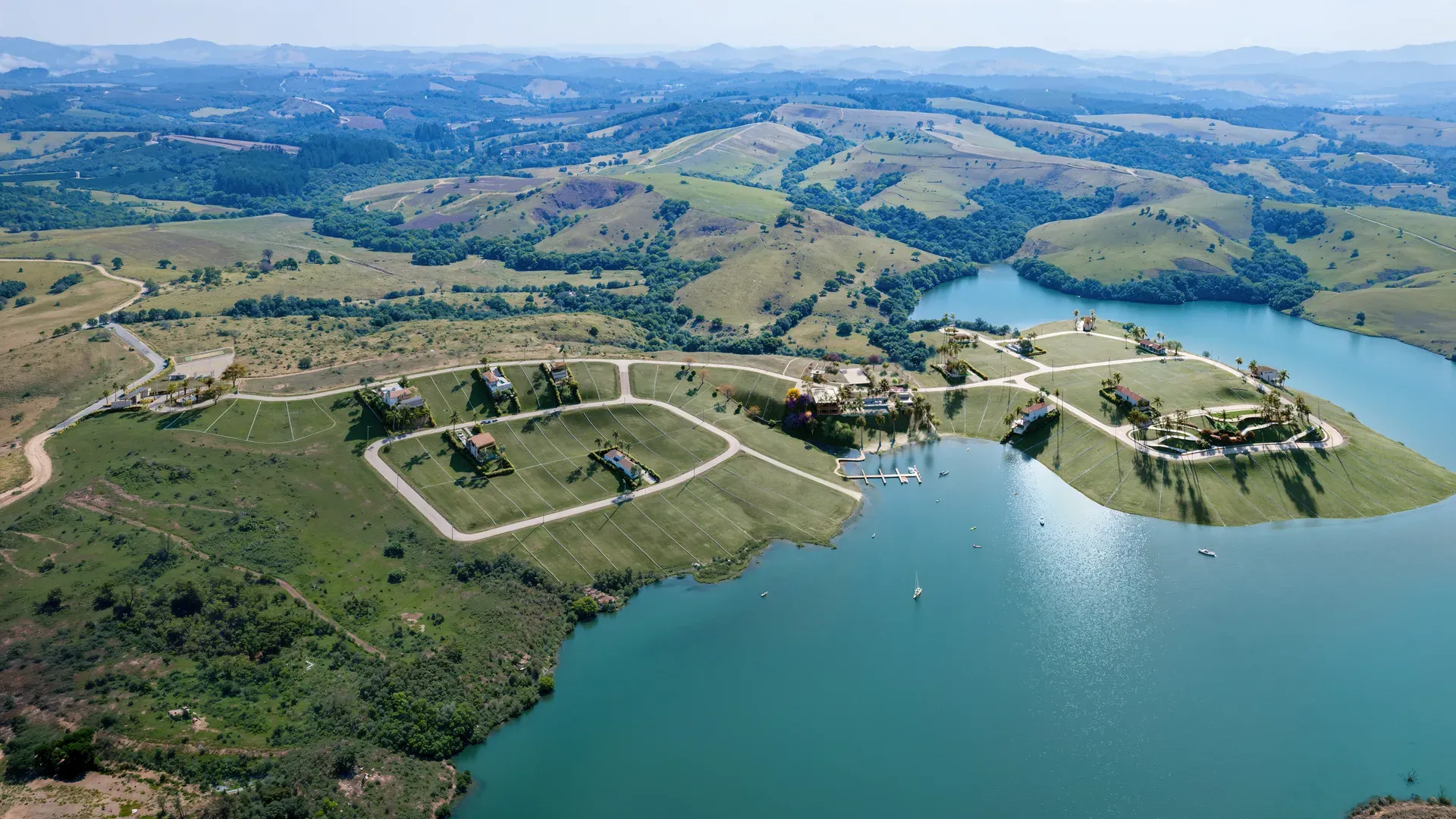 Vista aérea panorâmica do Porto Real Condomínio Náutico às margens do Lago do Funil em Perdões/MG, com a península do condomínio, o lago e a serra ao fundo.