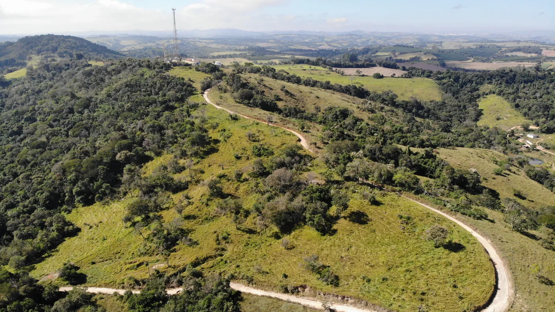 Área arborizada do Terreno Inhame com torre de telecomunicação na crista do morro e estradas de acesso