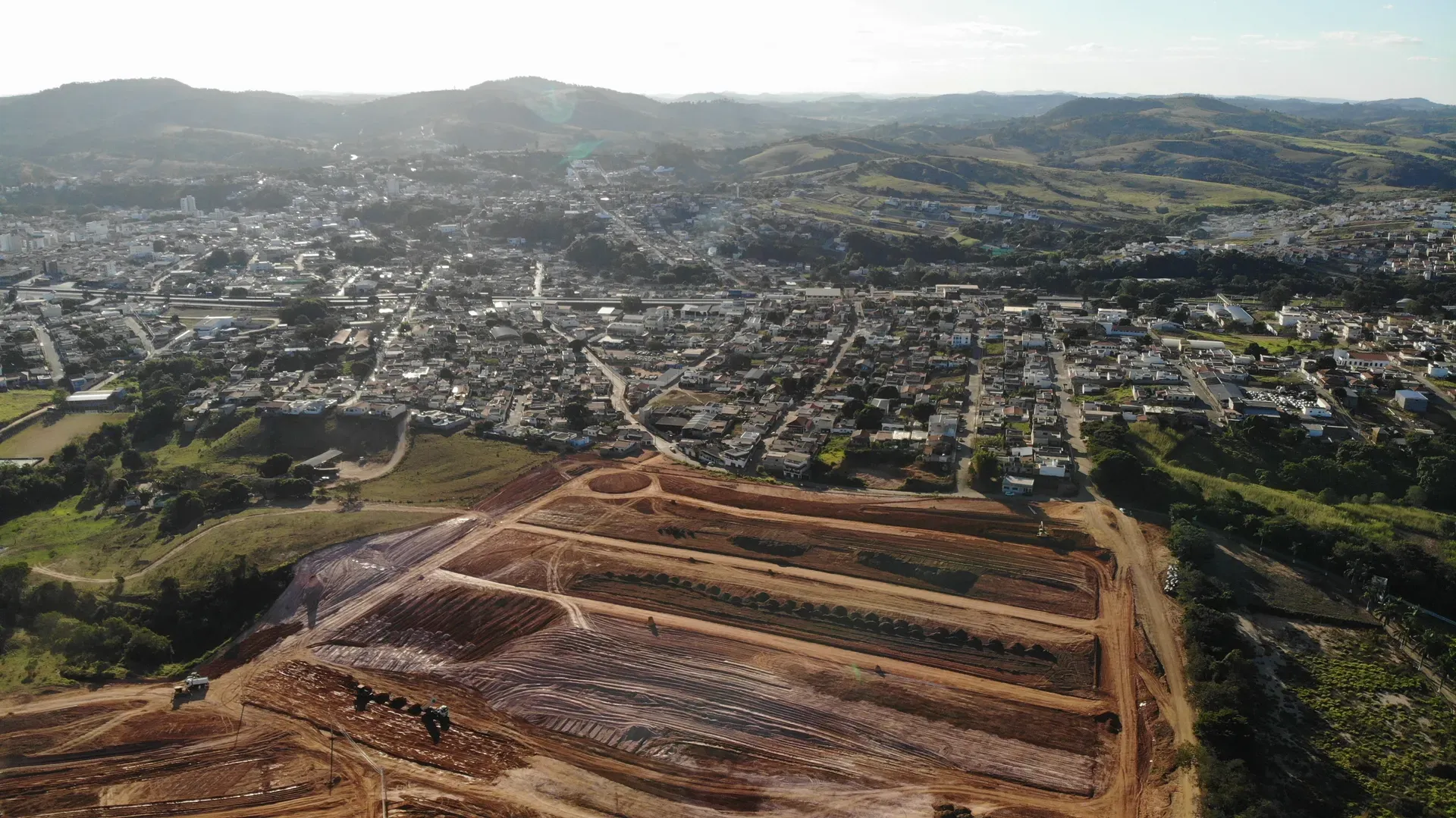 Vista aérea panorâmica do Portal da Serra em obras, com a malha urbana de Perdões ao entardecer
