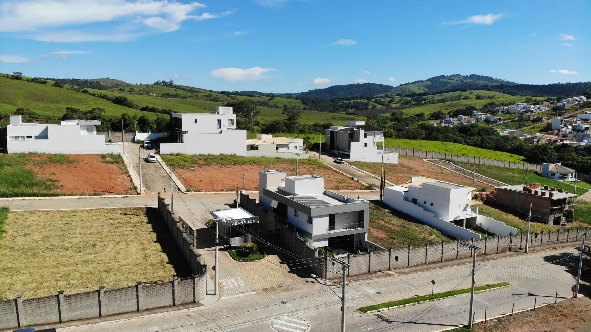 Portaria do Gran Ville com lotes ainda em construção, mostrando casas em diferentes fases de obra e a serra ao fundo