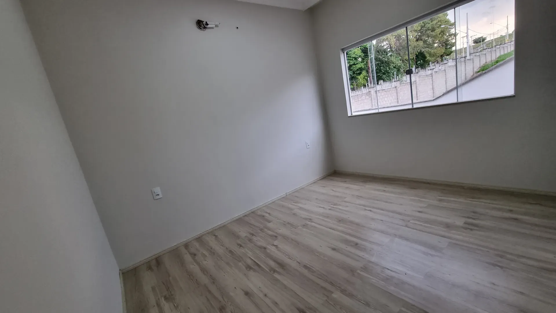 Segundo quarto da Casa do Gran Ville, com piso amadeirado e janela ampla com vista para o quintal