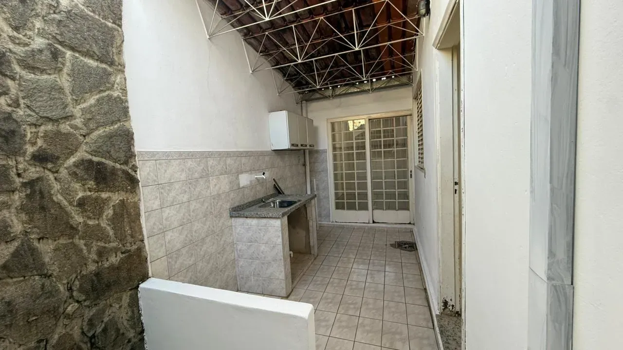 Área coberta da Casa do Lourdes, com pia em alvenaria, telhado aparente e porta de vidro de acesso