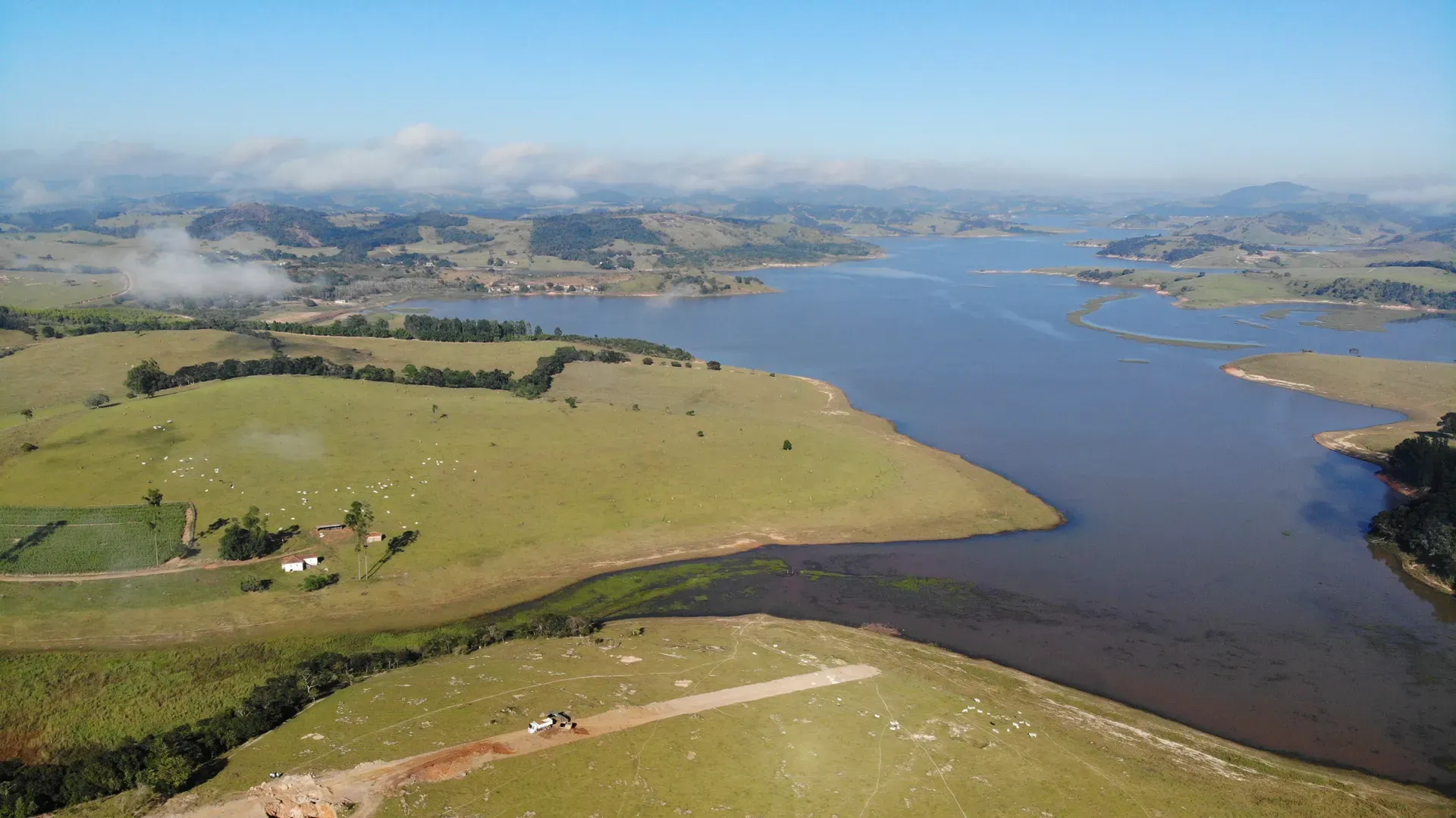 Enseada do lago junto às pastagens da Fazenda Coelhos, com a sede e o gado no pasto