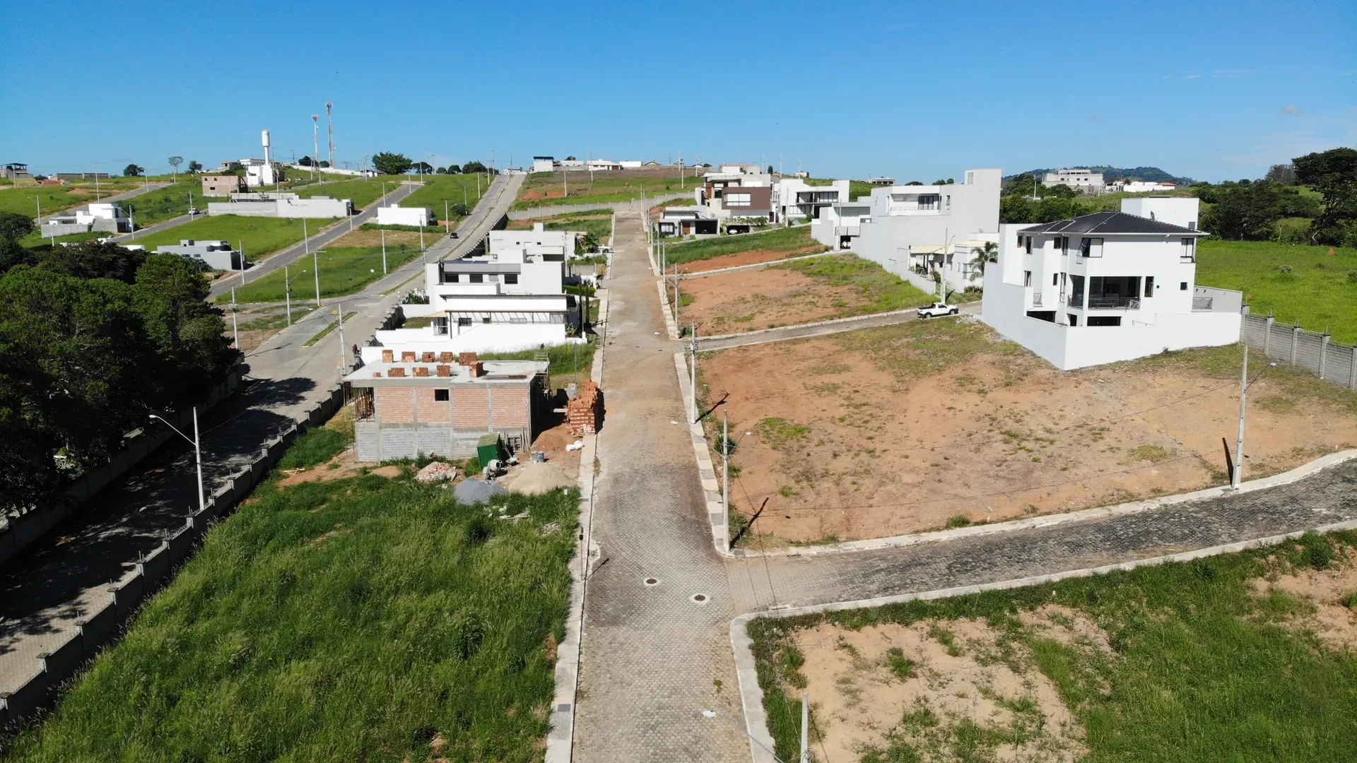 Rua interna do Gran Ville com lotes vagos e residências em diferentes estágios de construção, vista lateral do conjunto