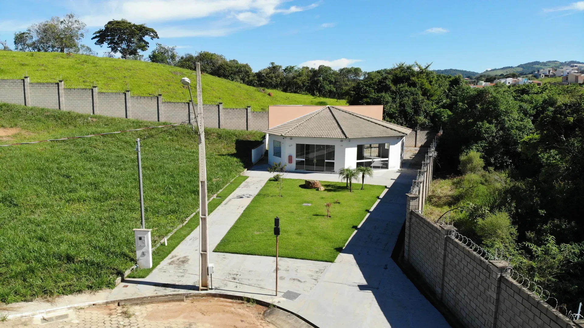 Fachada frontal do amplo salão de festas do Gran Ville, com jardim, calçamento e cerca de perímetro