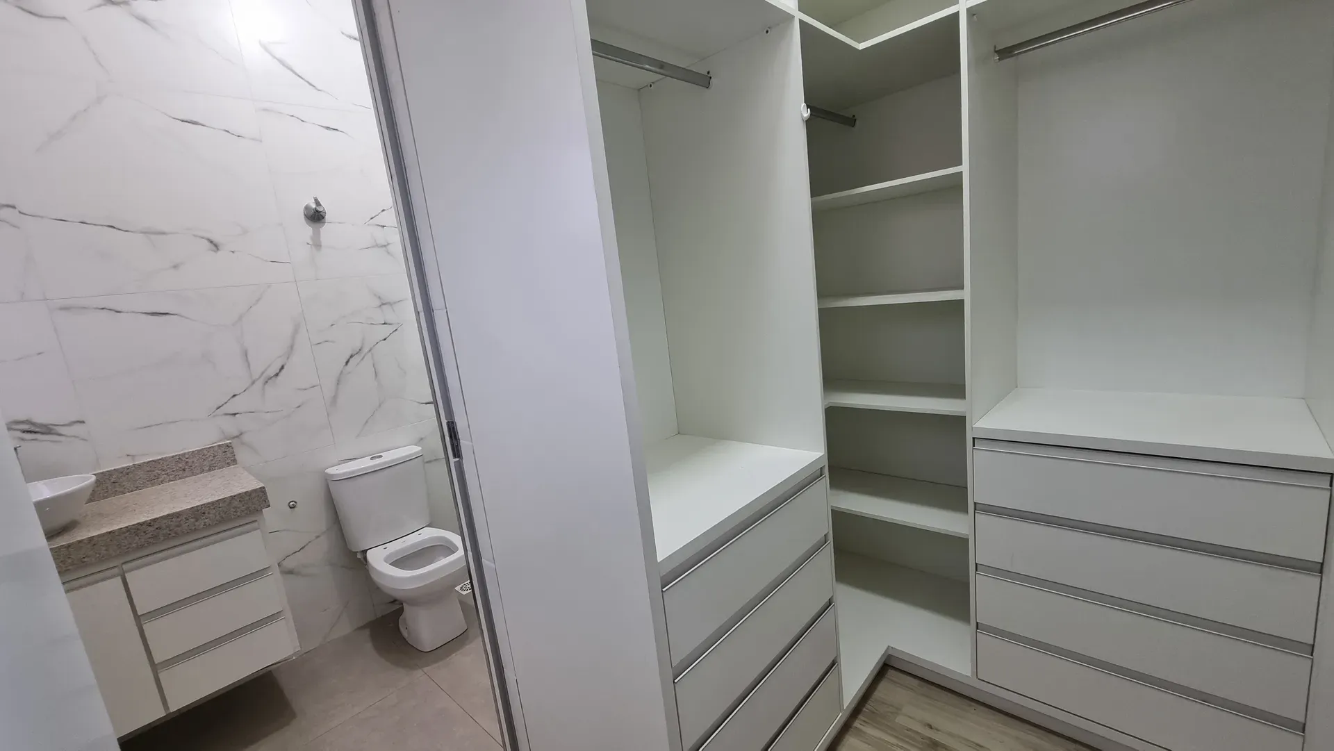 Banheiro da suíte da Casa do Gran Ville, com revestimento marmorizado, bancada com cuba e closet integrado