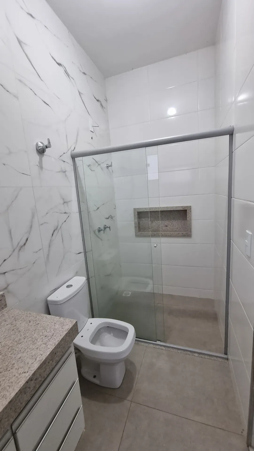Banheiro da Casa do Gran Ville com box de vidro amplo, nicho embutido e piso marmorizado