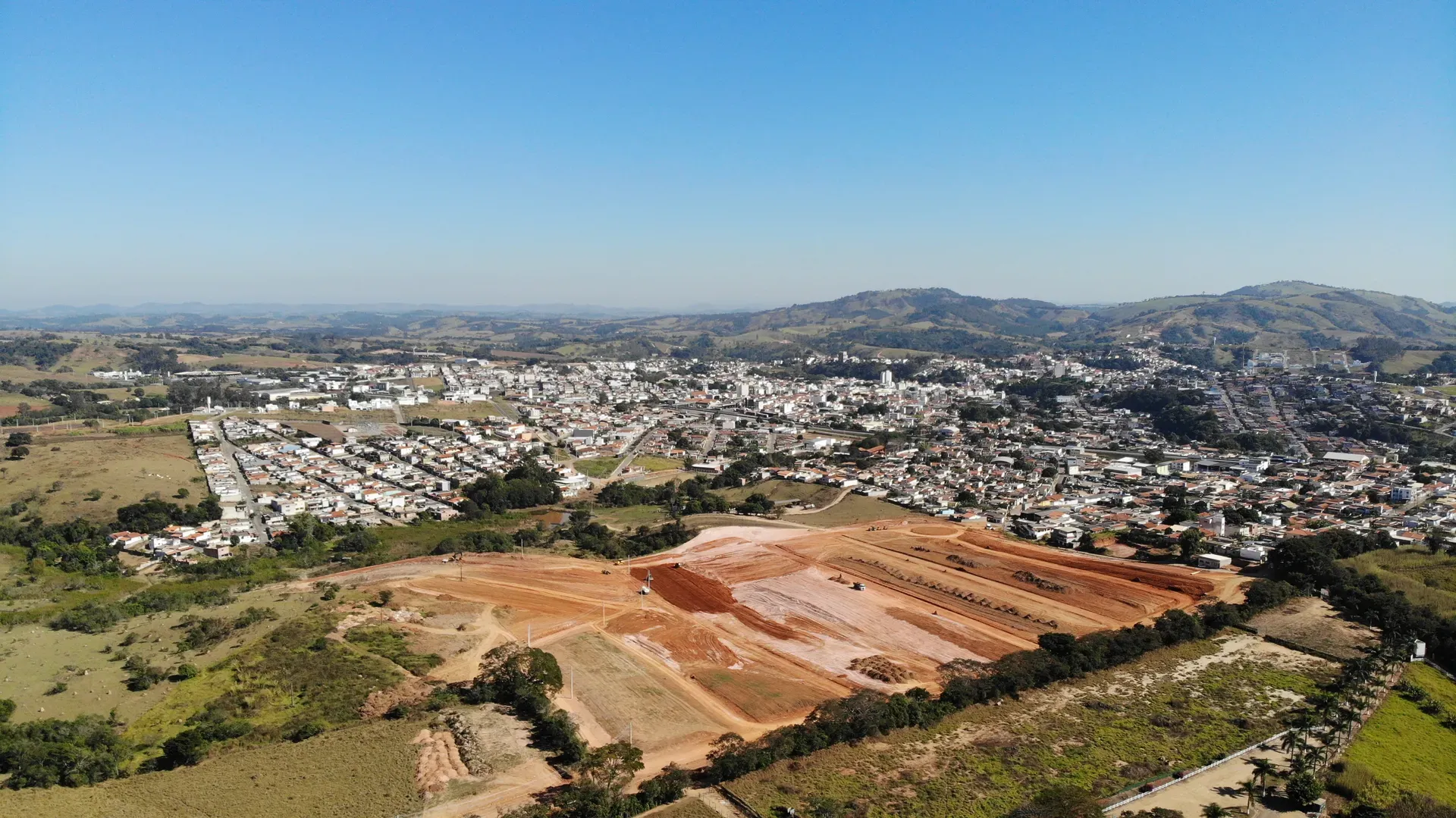 Vista aérea regional do Portal da Serra em obras, com Perdões e o relevo do Sul de Minas