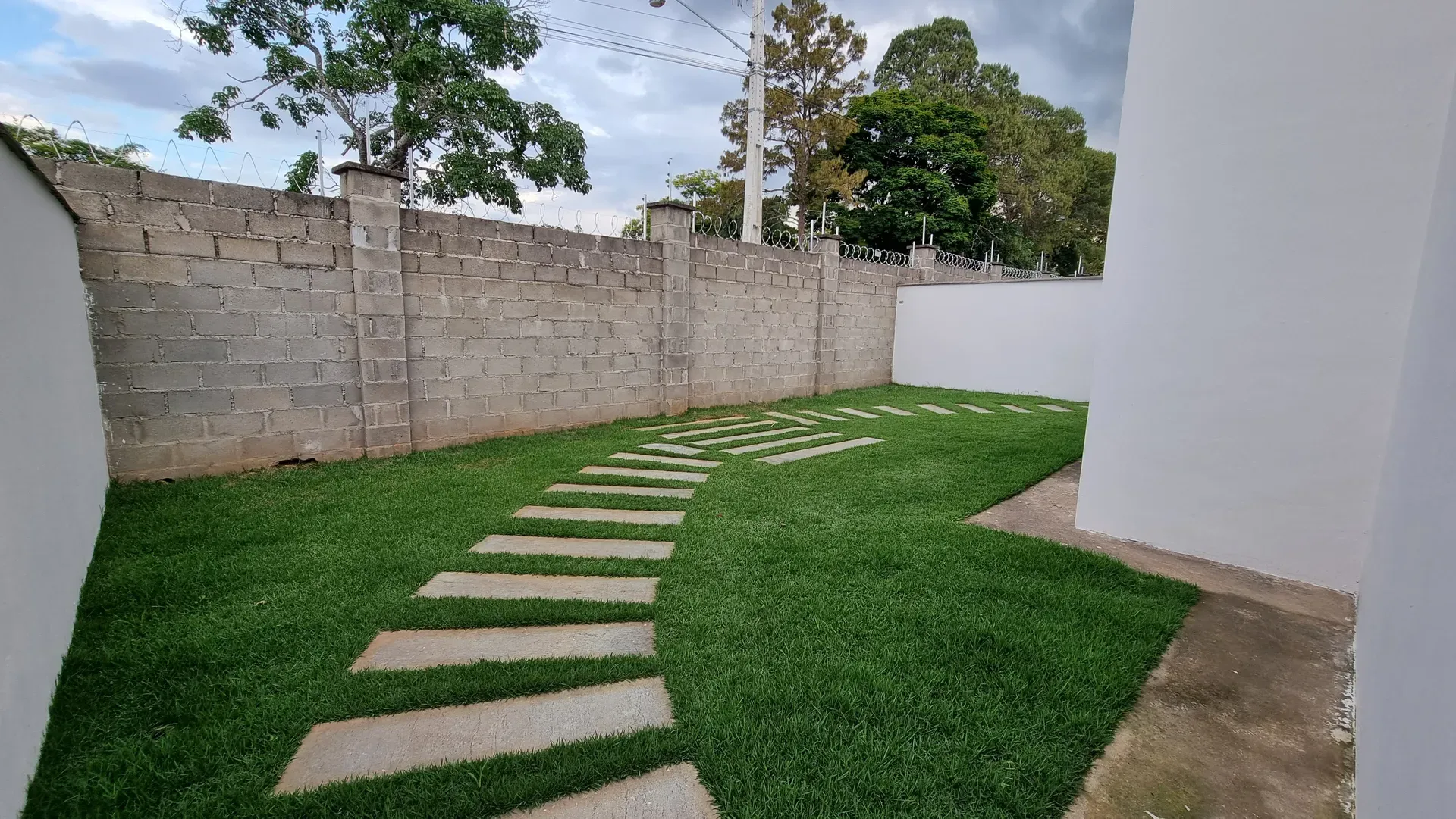 Quintal gramado da Casa do Gran Ville, com caminho de pedras e muro de divisa