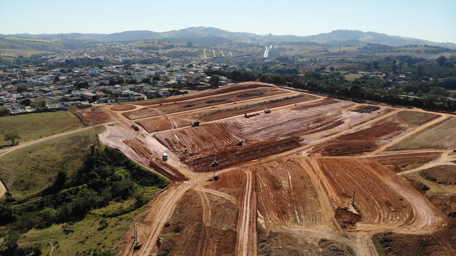 Vista aérea do Portal da Serra mostrando os acessos e os platôs do loteamento em terraplenagem, com a cidade ao lado