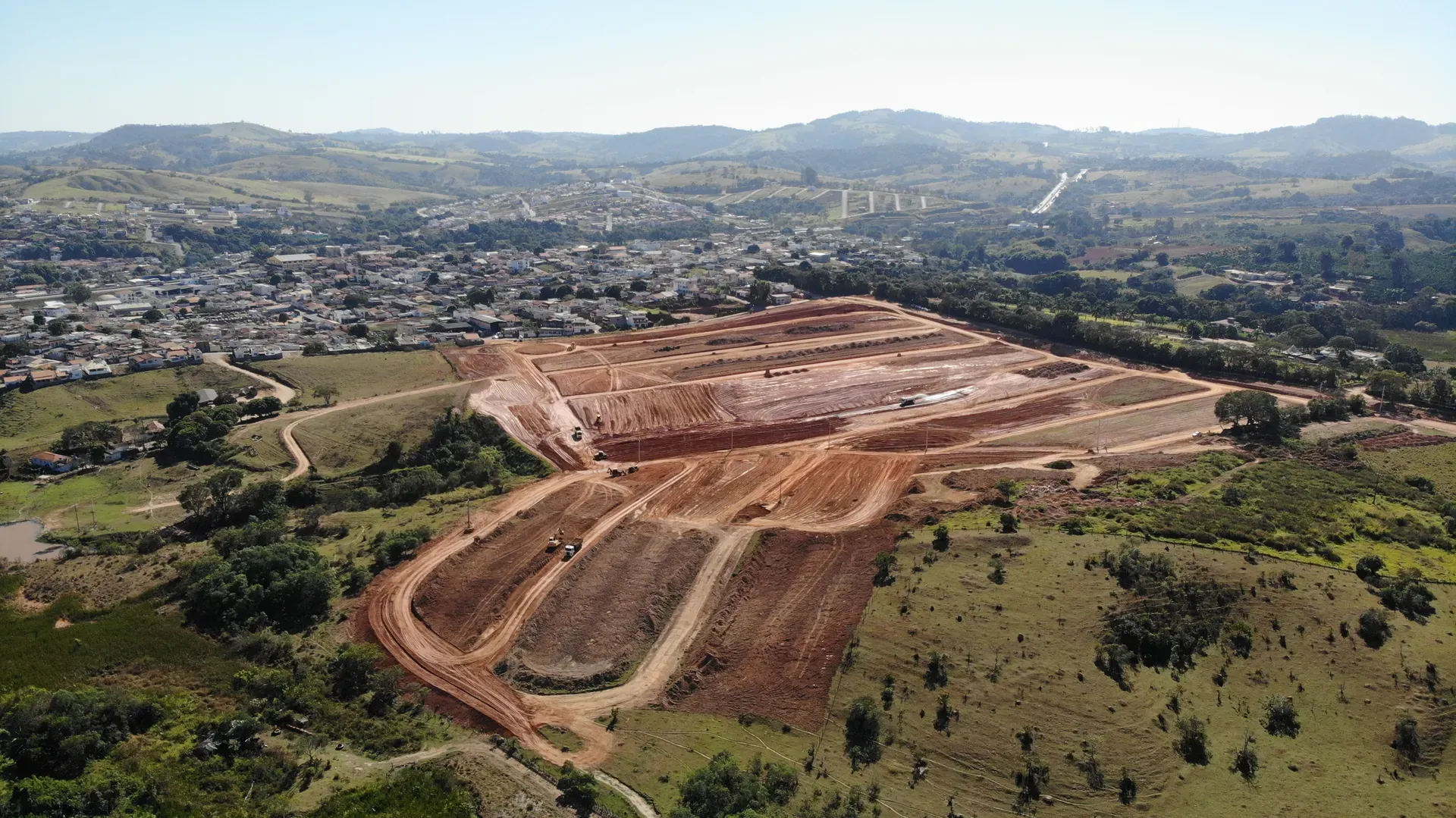 Vista aérea do loteamento Portal da Serra em obras, com os acessos demarcados e a serra do Sul de Minas ao fundo