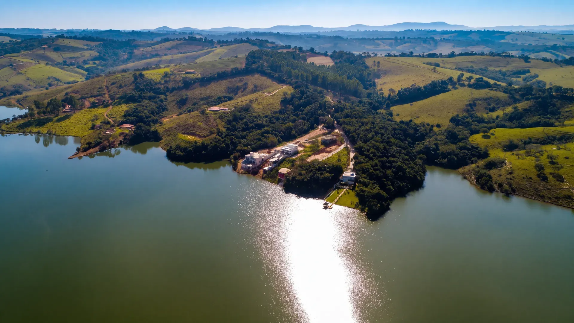 Vista aérea panorâmica do Condomínio Estância do Funil em Perdões/MG, com a península do condomínio ao centro, a Represa do Funil ao redor e a serra ao fundo