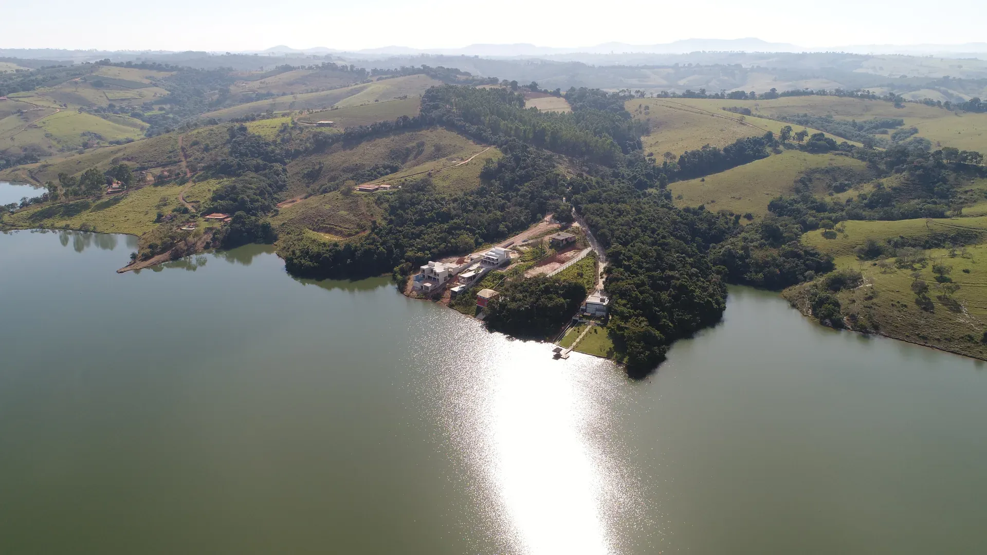 Vista aérea panorâmica do Condomínio Estância do Funil em Perdões/MG, com a península do condomínio ao centro, a Represa do Funil ao redor e a serra ao fundo