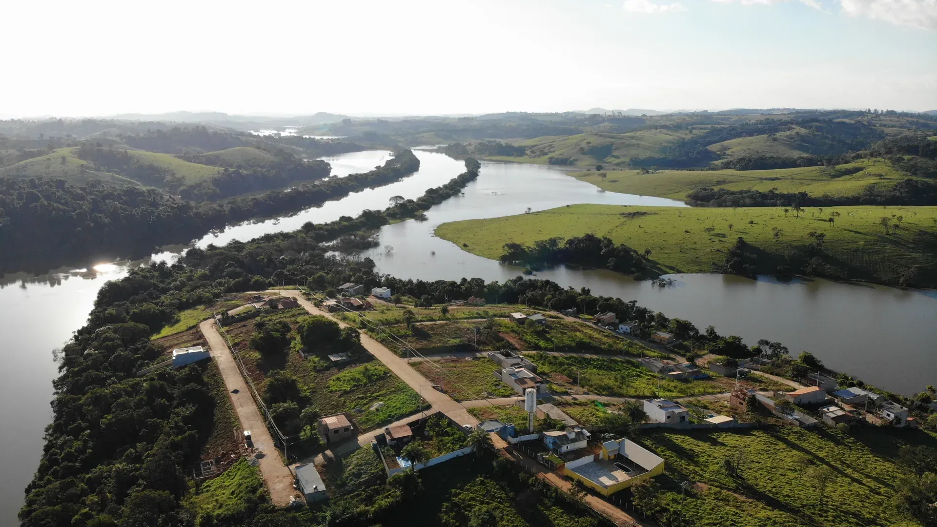 Vista aérea do Condomínio Portal do Lago às margens do Rio Grande em Perdões/MG, com o rio serpenteando entre as colinas verdes e os lotes do condomínio na margem