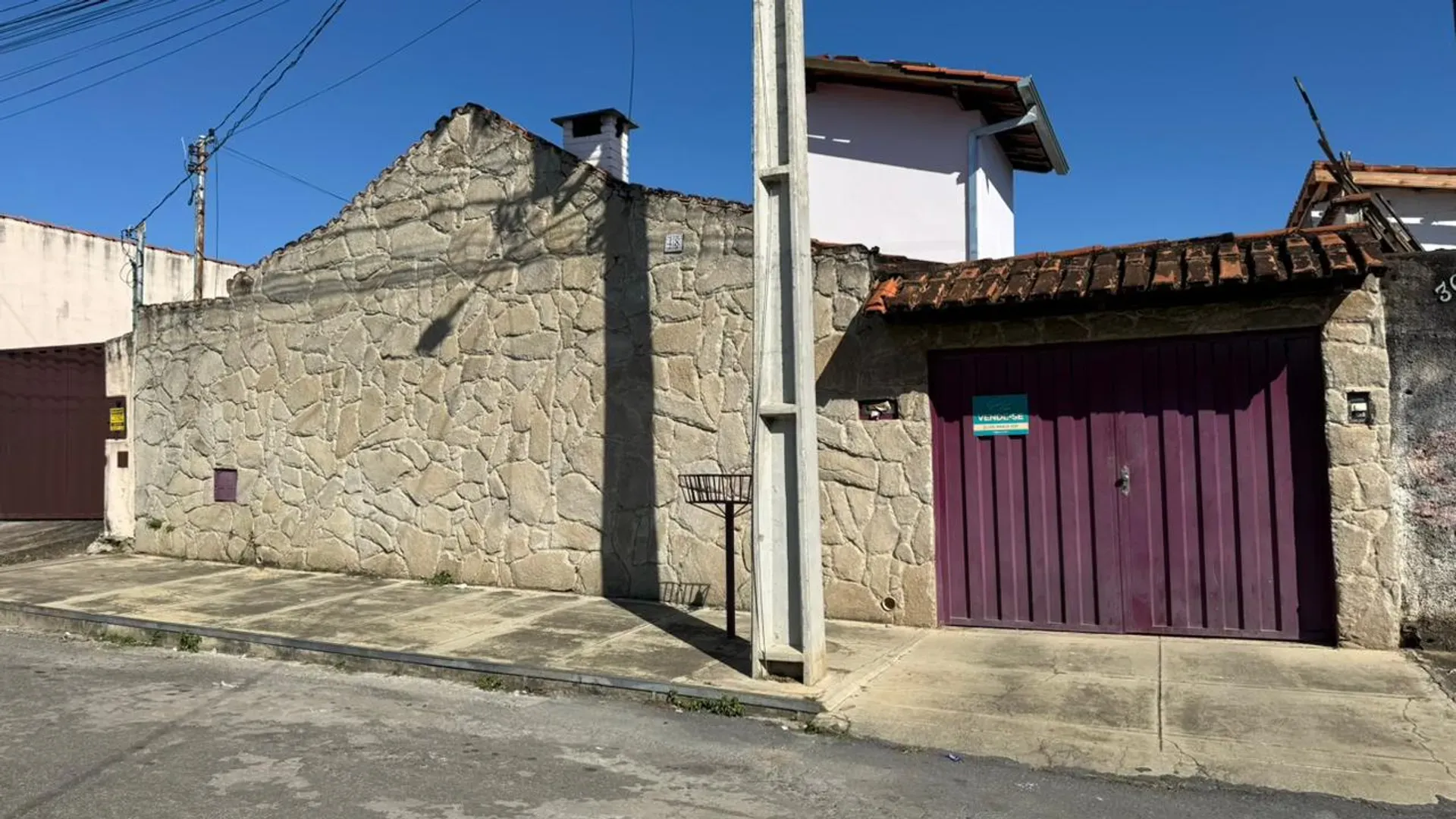 Fachada da Casa do Lourdes vista da rua, no bairro Nossa Senhora de Lourdes em Perdões/MG, com muro de pedra e portão de garagem