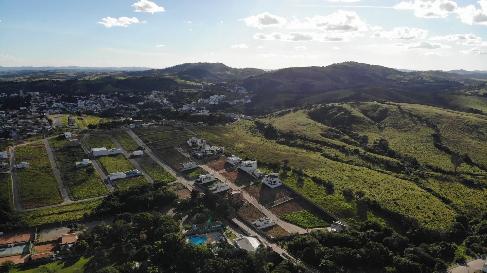 Vista aérea do Condomínio Gran Ville em Perdões/MG ao entardecer, com lotes e casas residenciais integrados entre a cidade e a serra
