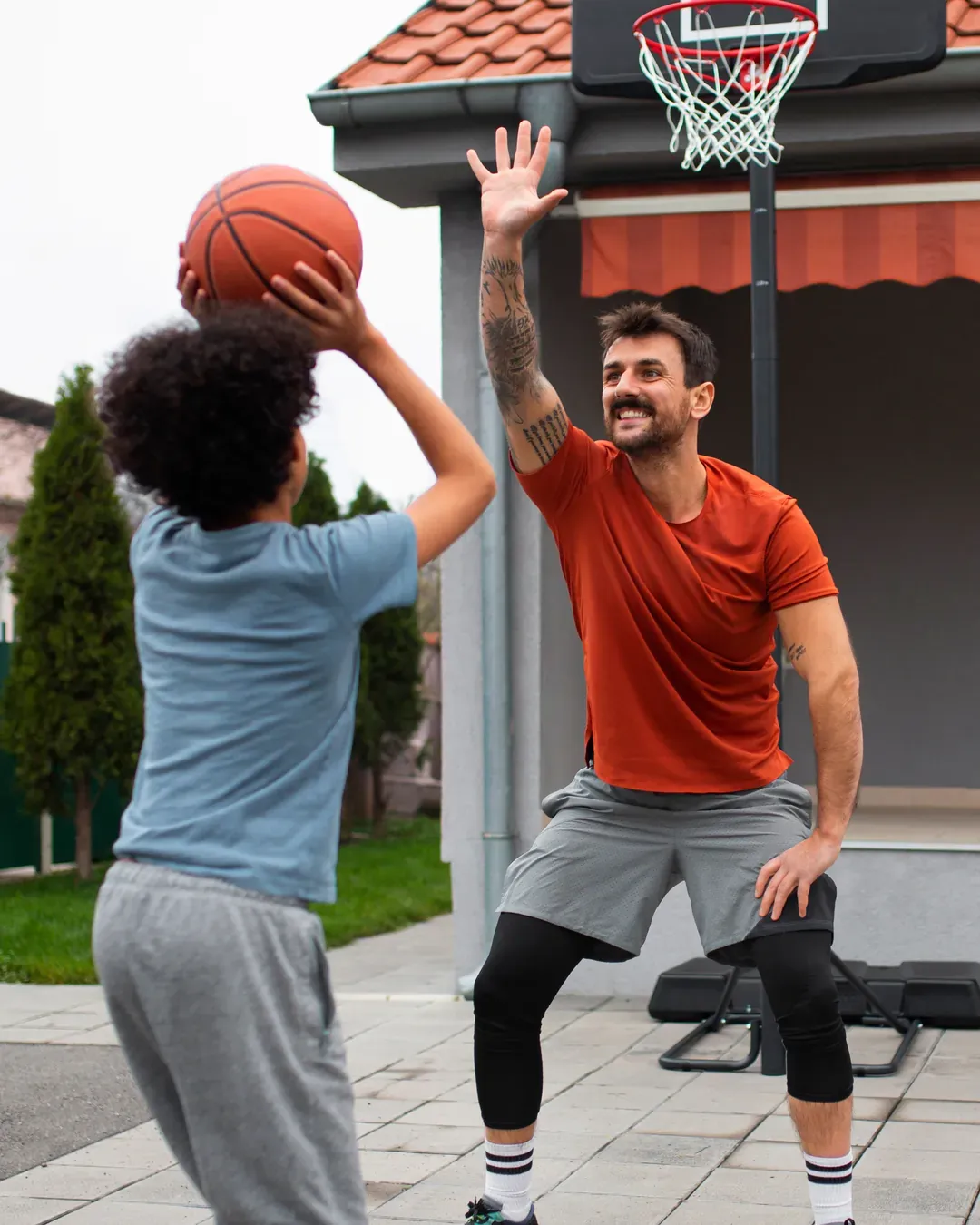Pai e filho jogam basquete na frente de casa, com a cesta presa à fachada